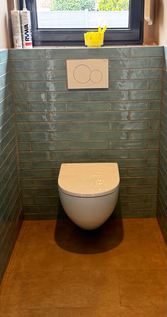 Nachher: fertig gefliestes Bad in Grüntönen mit wandhängendem WC.