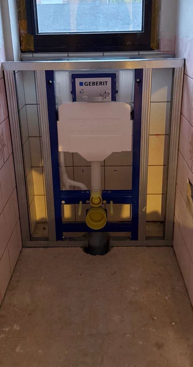 Vorher: freigelegte Geberit-Vorwandinstallation in einem alten Bad mit rosa Fliesen.